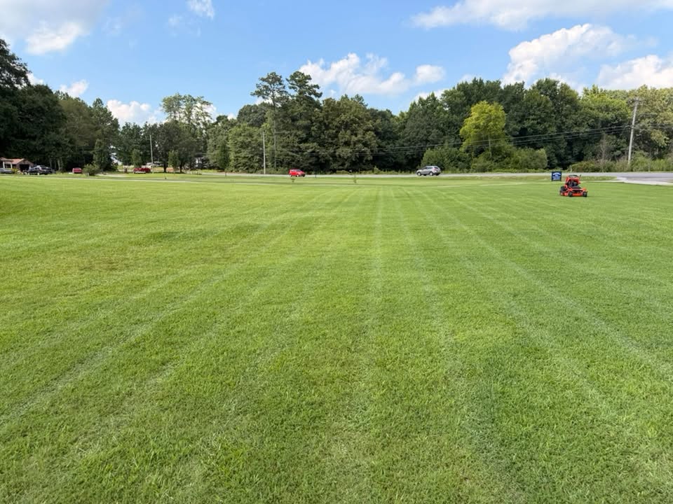 Freshly striped green field with a mower in the distance